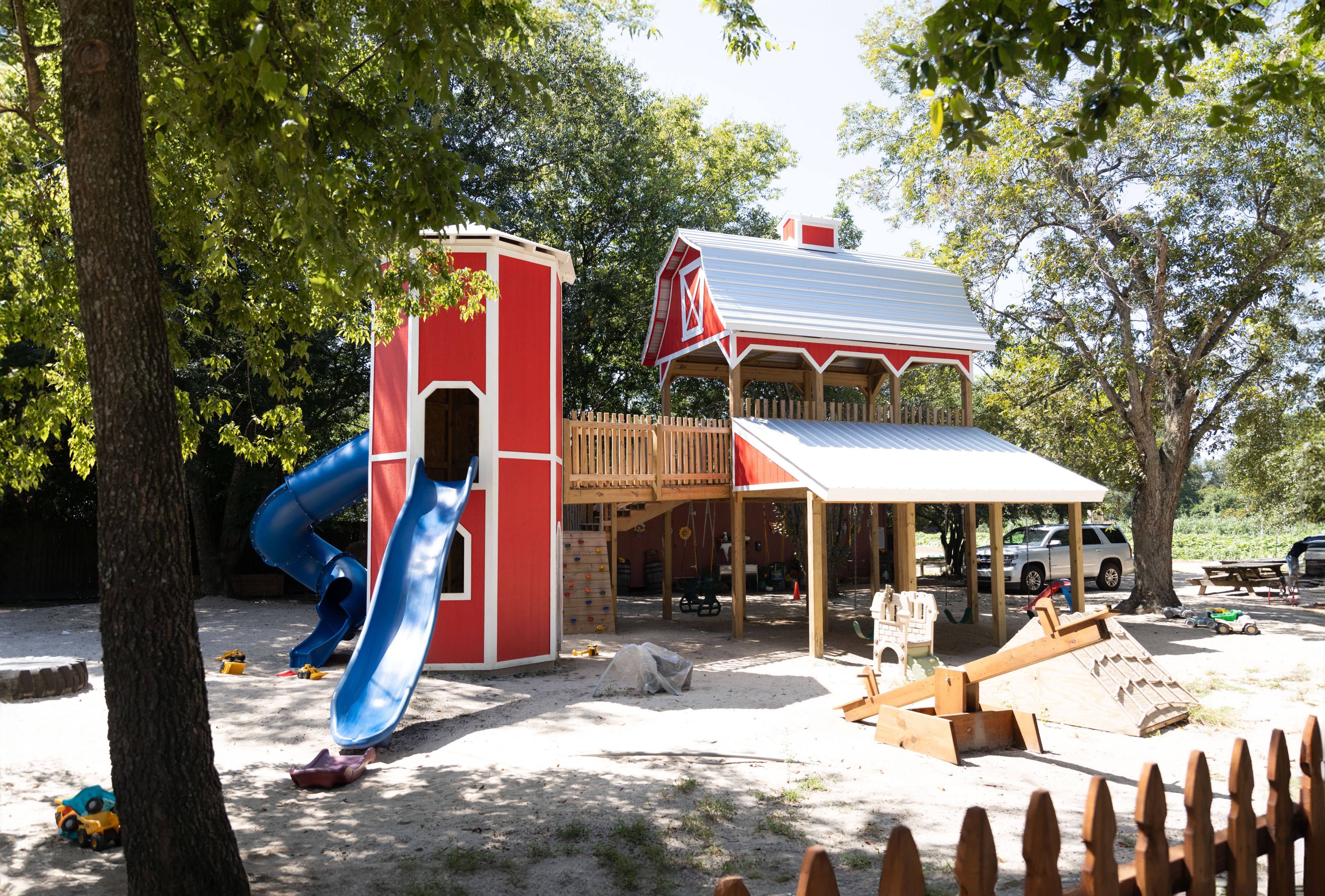 A red and white playground that looks like a barn, with two blue slides and trees in the background.