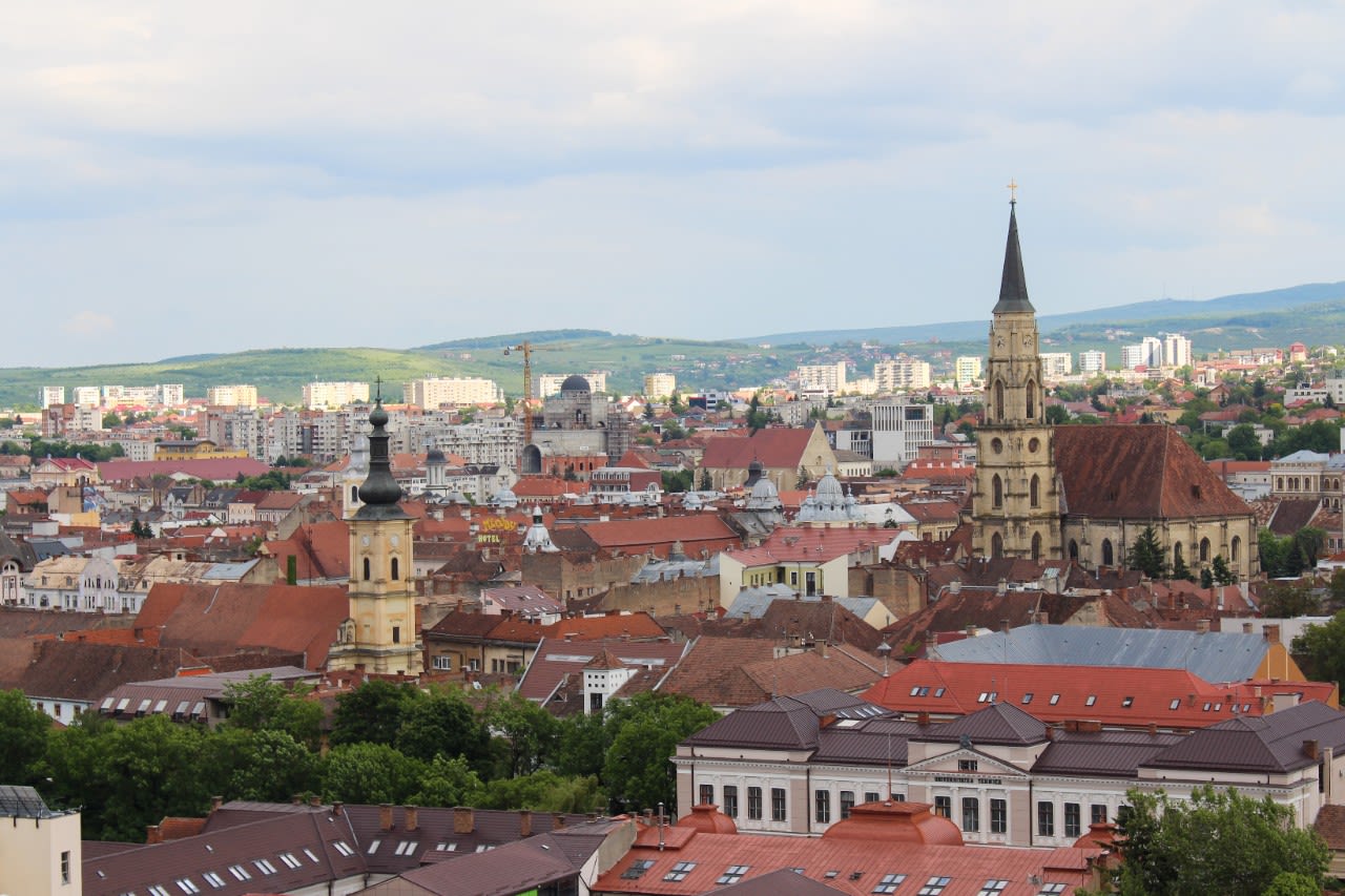 View of a Romanian city shows red rooftops and green rolling hills in the backbground