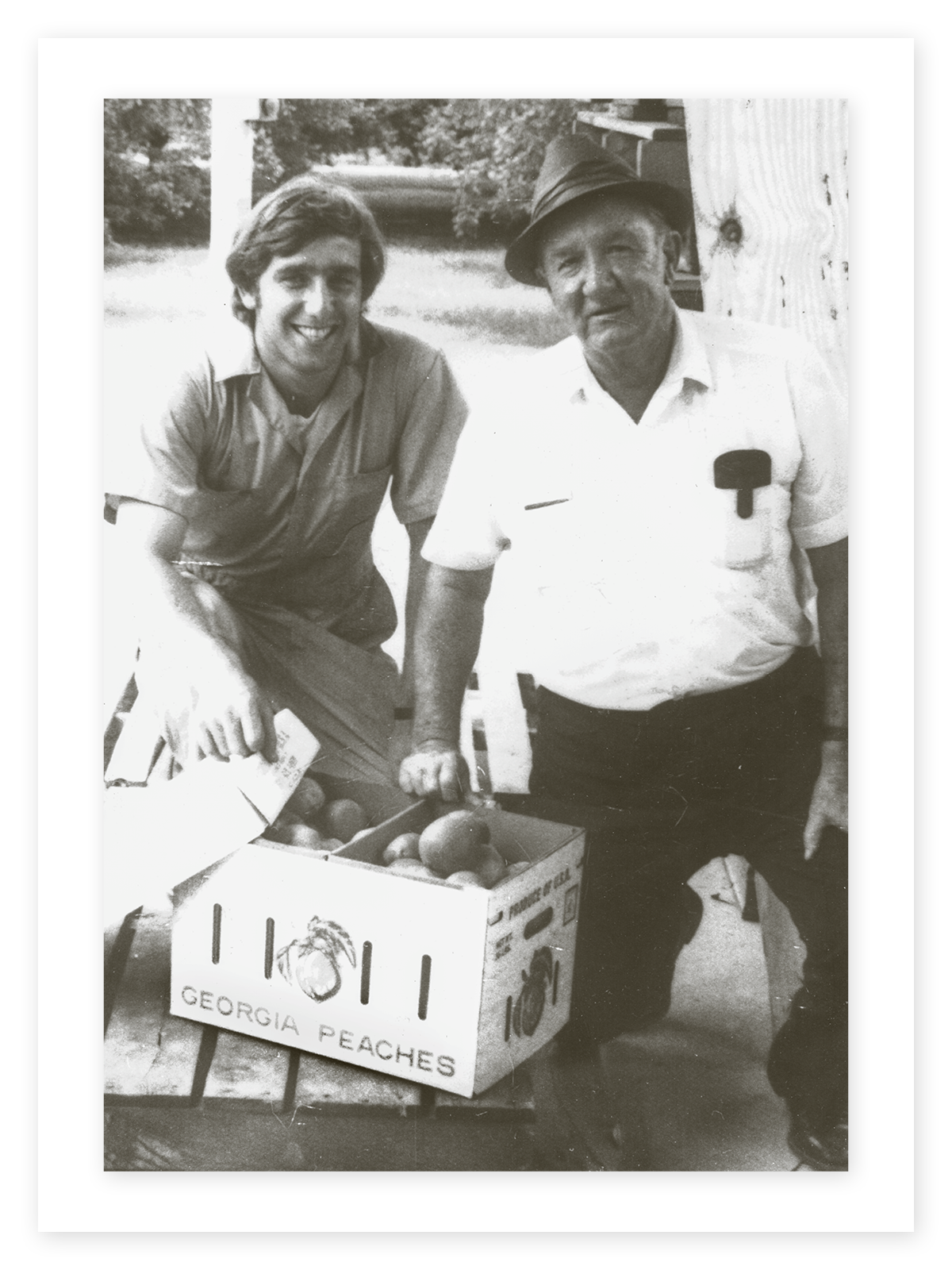 In a sepia-toned photo, Al Pearson (left) smiles with his father, Lawton Pearson, with a crate of peaches in the foreground