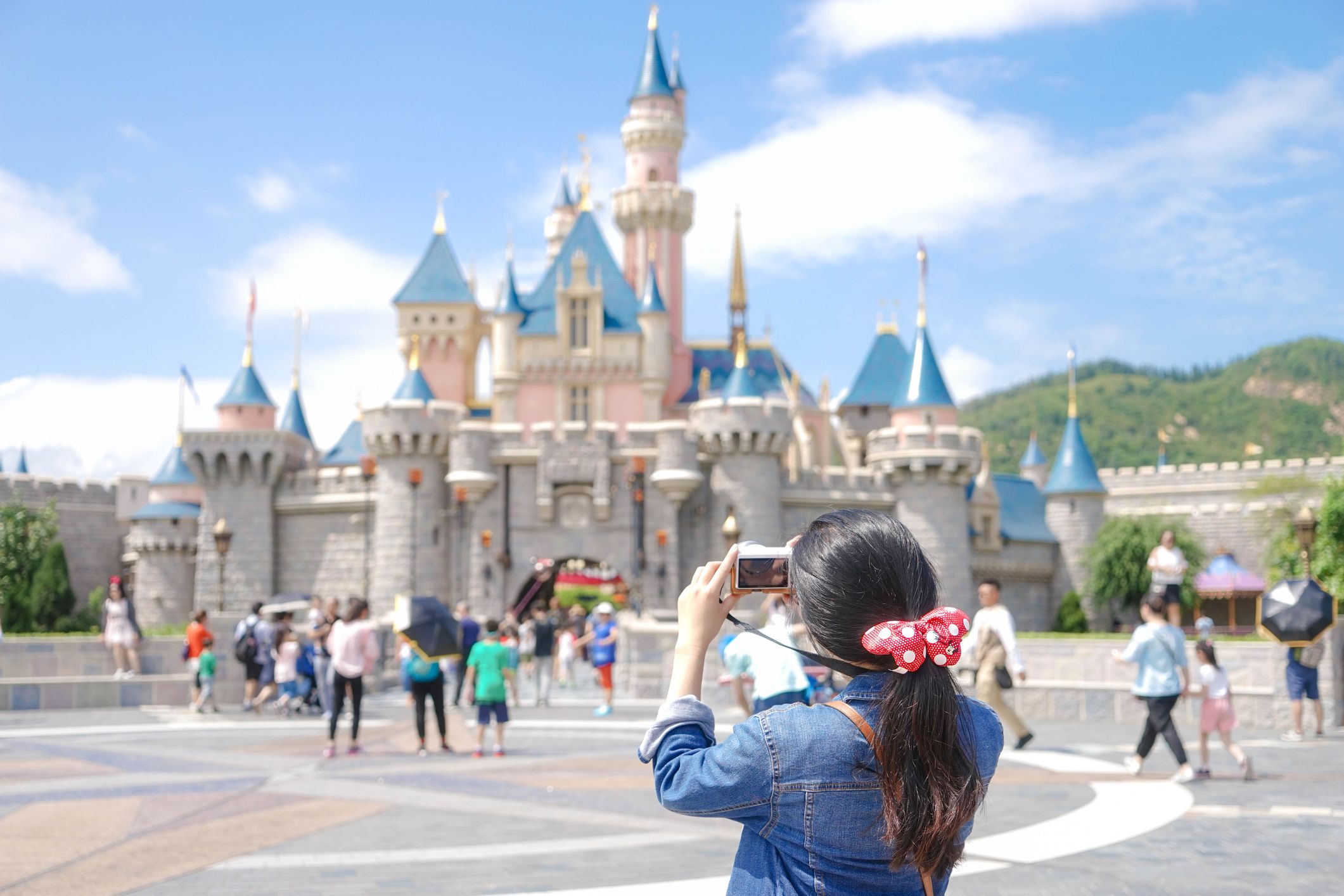 A girl with dark hair and a red polka dotted bow takes a photo of the castle in Disney's Magic Kingdom