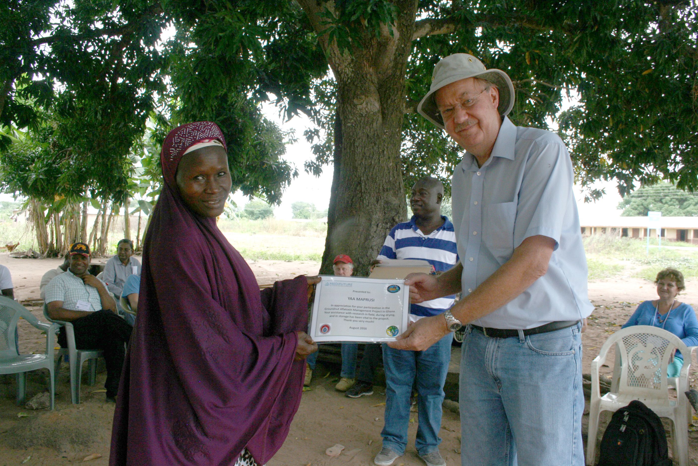 Hoisington presents a Ghanaian farmer with a certificate, with other participants sitting on outdoor chairs in the background
