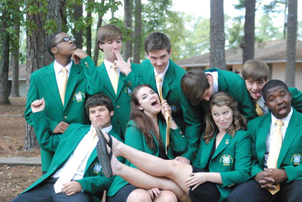 Erin White (second from right, front row) and eight other 4-H'ers wearing green 4-H blazers do silly poses for the camera in a camp setting