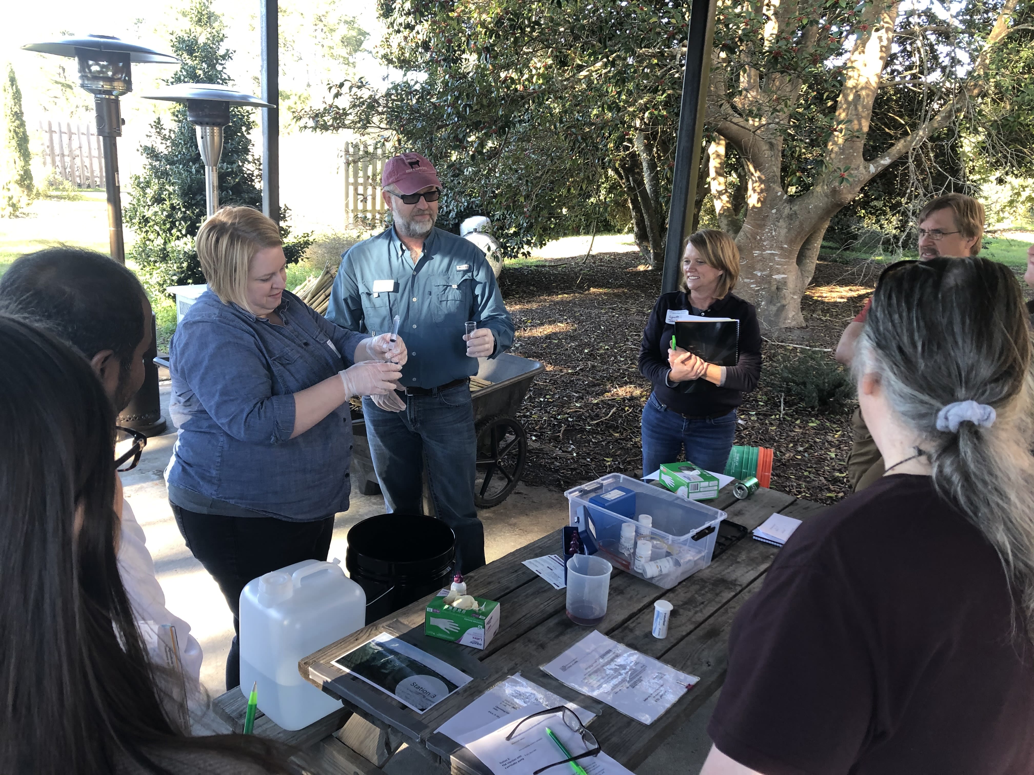 In an outdoor setting with a folding table, Associate Professor Faith Critzer training other Extension educators on how to conduct a titration to monitor sanitizer concentrations.