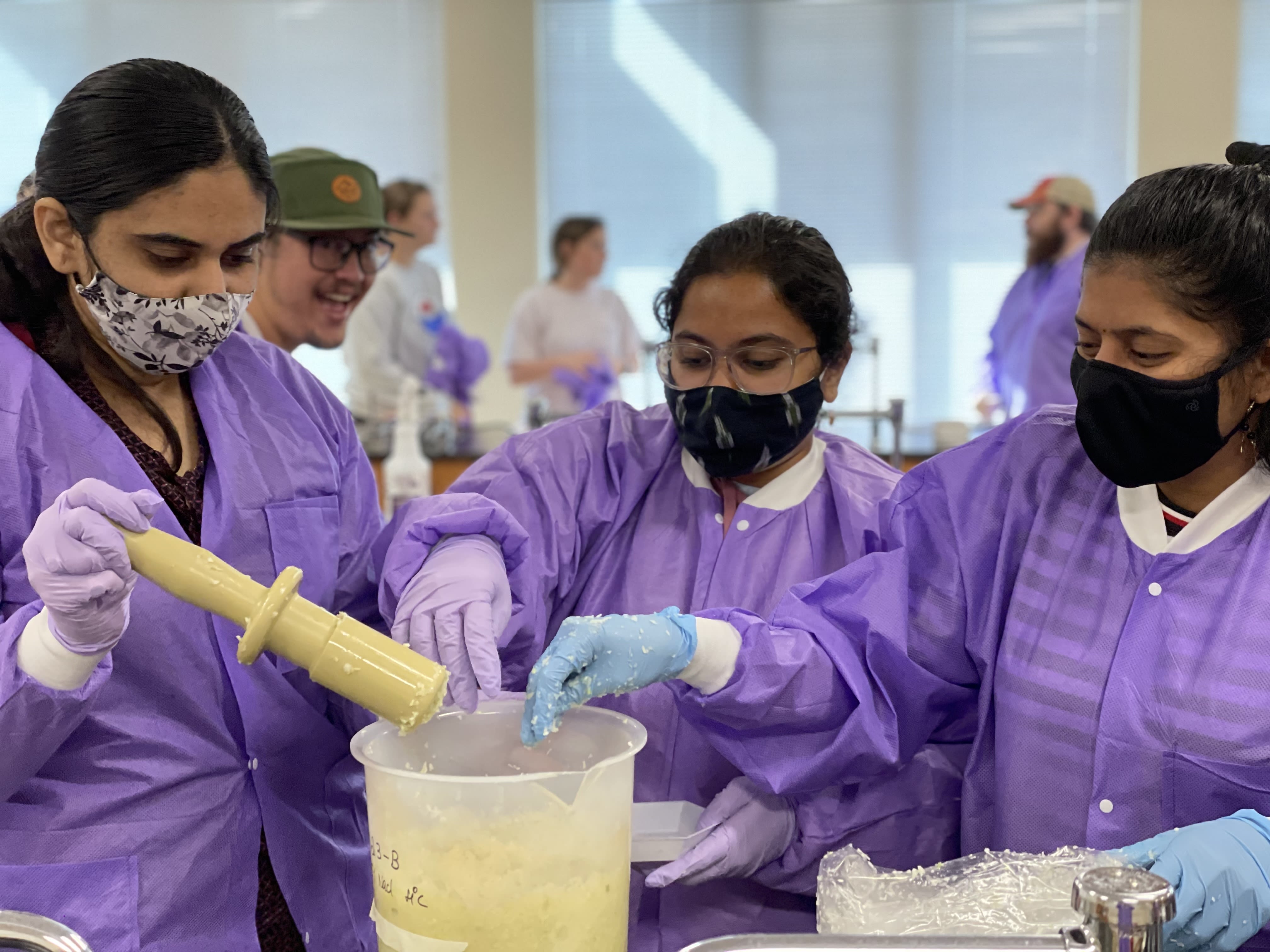 Students in purple protective outerwear and face masks work in a lab