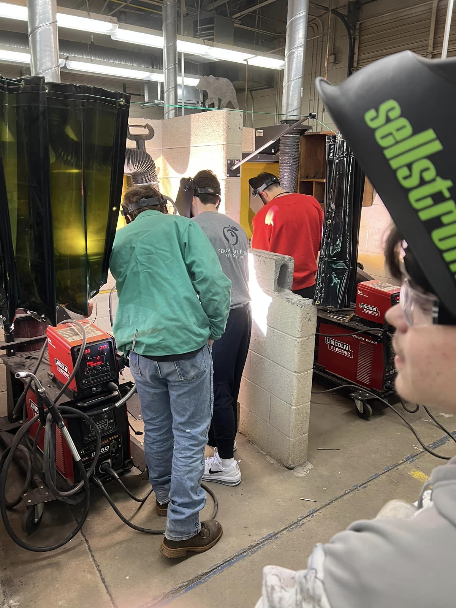 Four students wearing protective gear learn arc welding in the shop