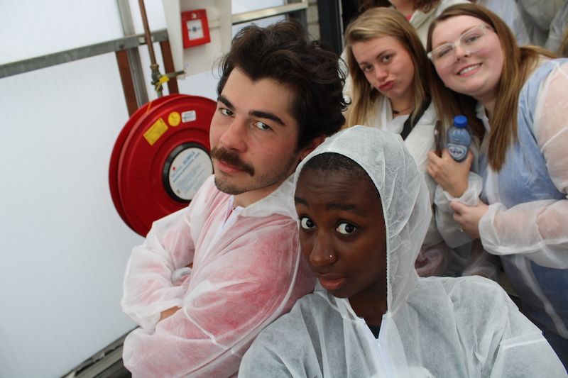 Four students pose for an overhead selfie while wearing PPE in a greenhouse