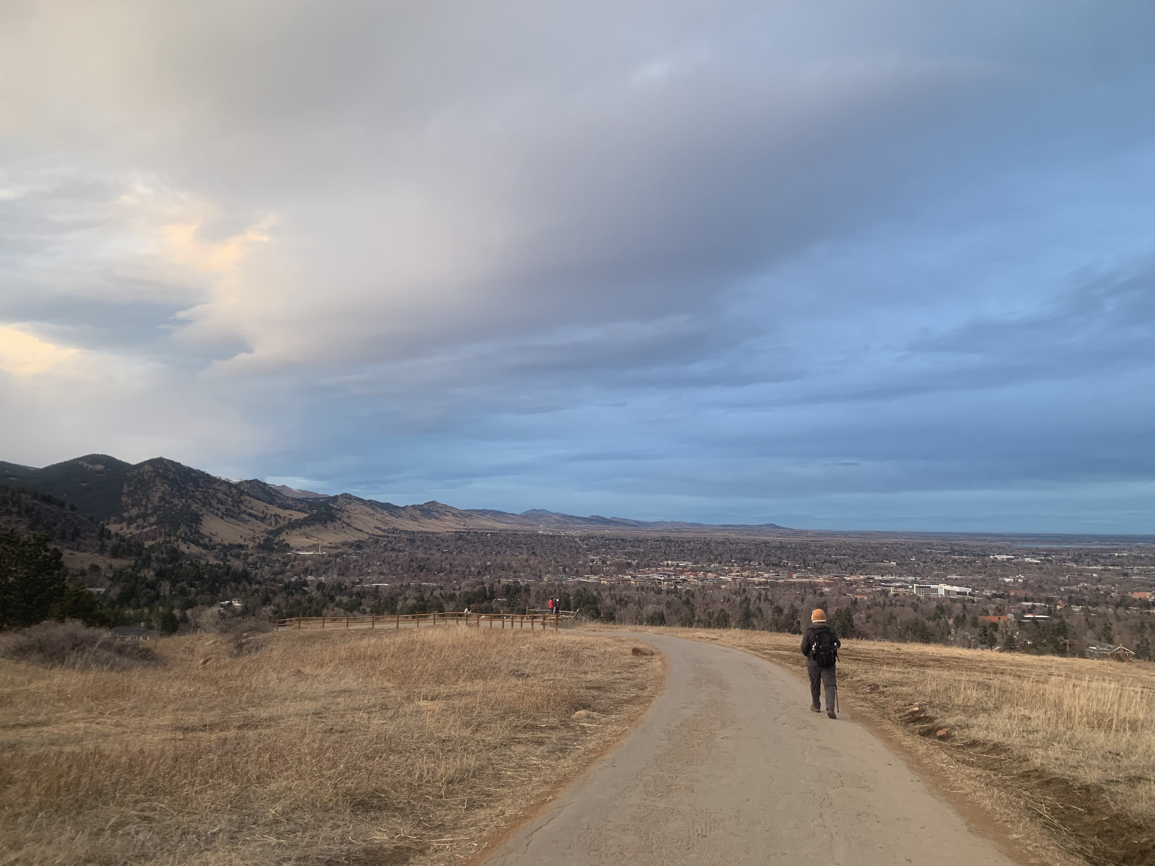A person hiking away from the camera with mountains in the background under a blue sky.