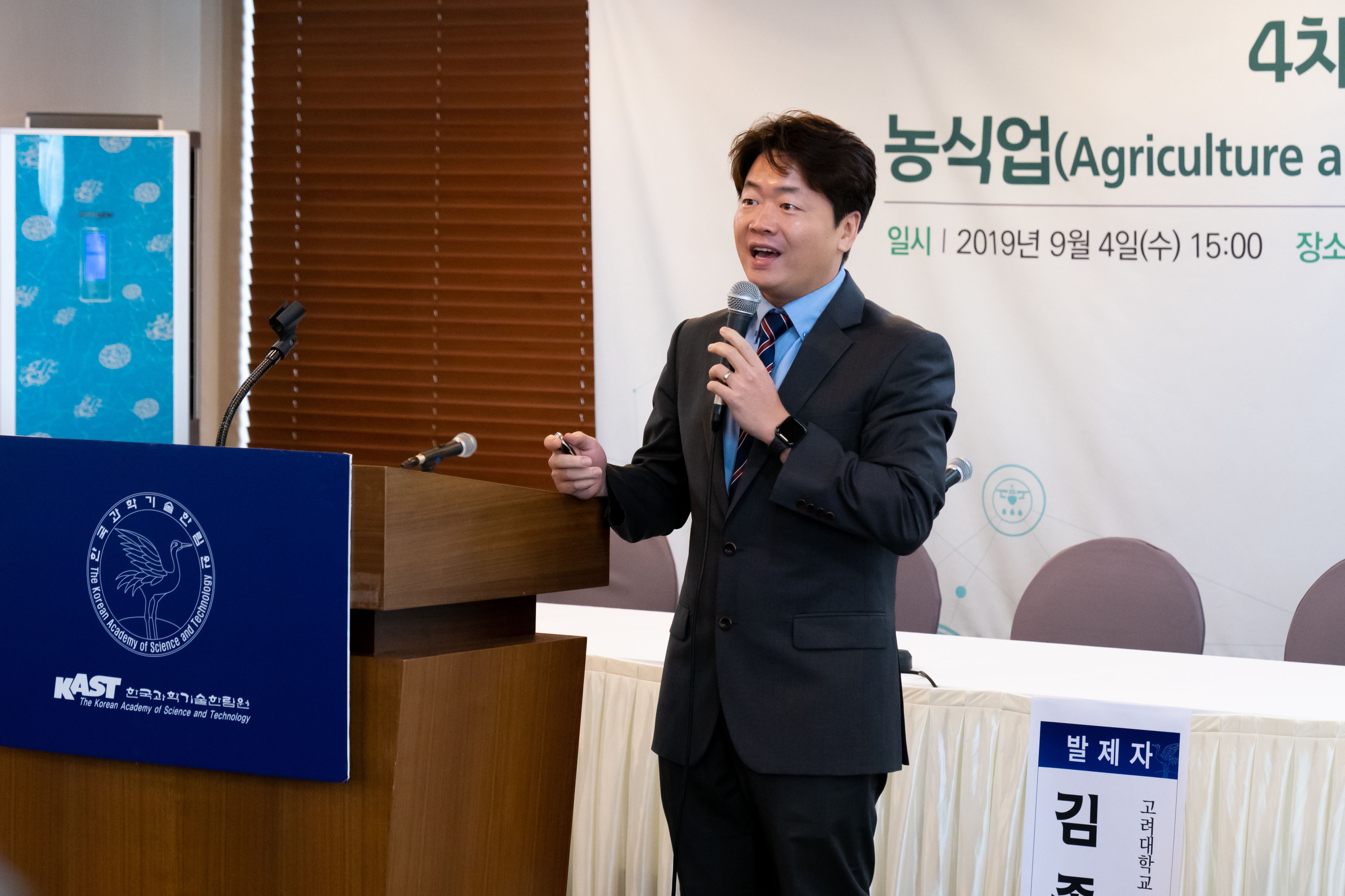 Jongyun Kim stands at a Korean Academy of Science and Technology-branded lectern with a microphone speaking on “The 4th Industrial Revolution and Agriculture.”