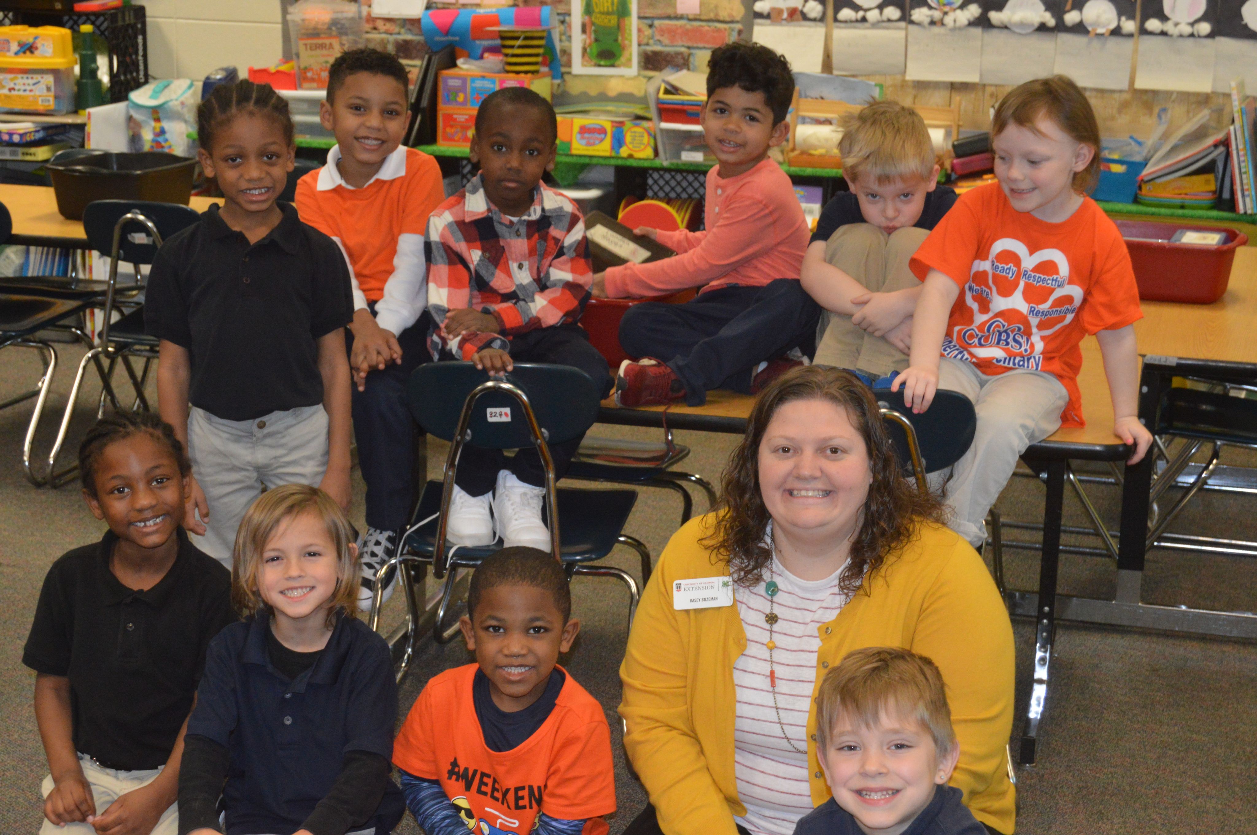 Kasey Bozeman sitting with 10 schoolchildren in a classroom setting