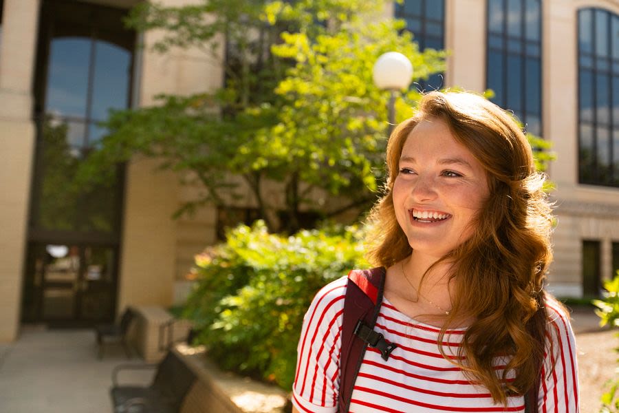 Kylie Bruce smiles in front of Conner Hall on UGA's South Campus. She is wearing a striped shirt and a backpack