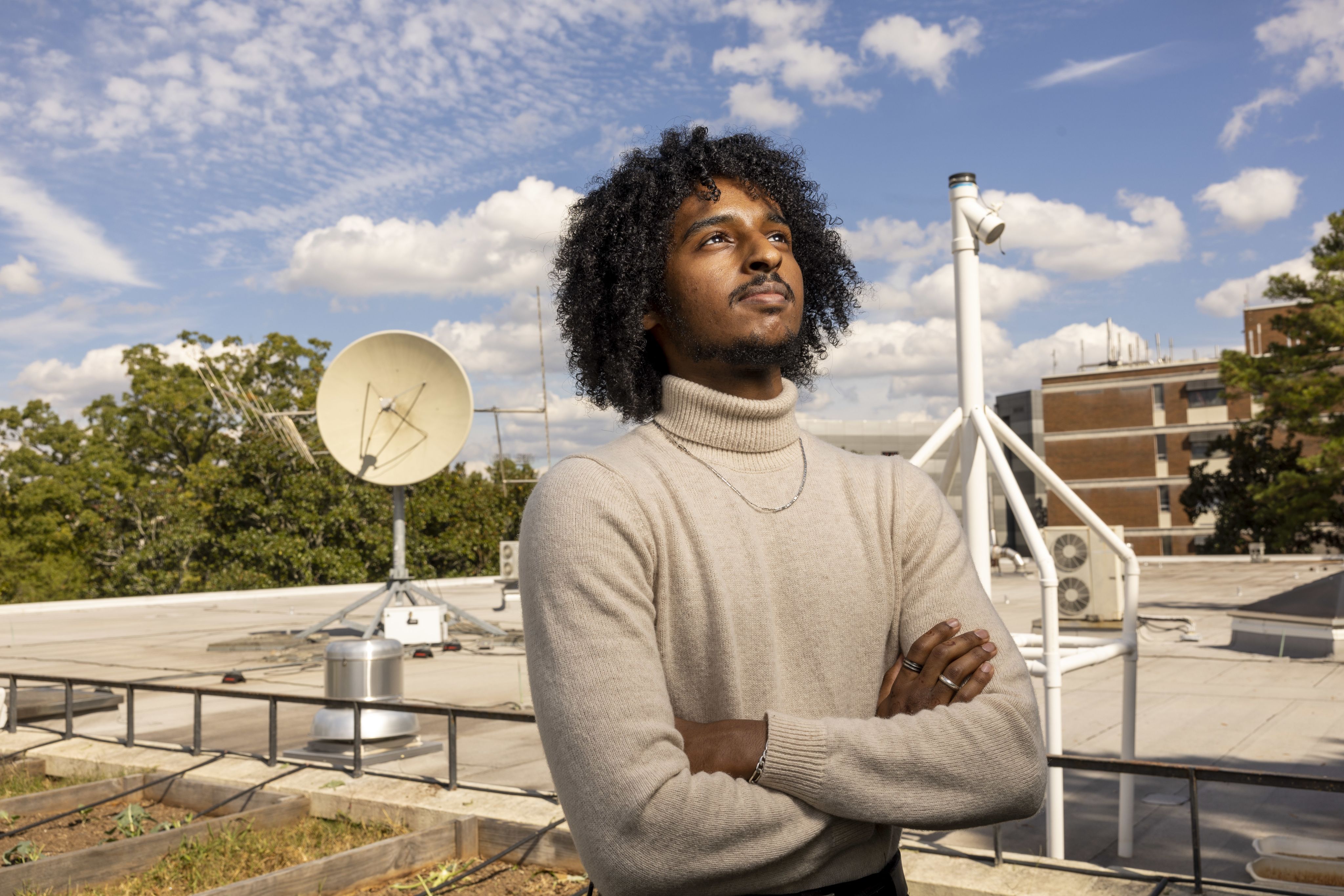 Nathan Tesfayi looking off to the distance. He is stood on a roof the sky is visible behiind him.