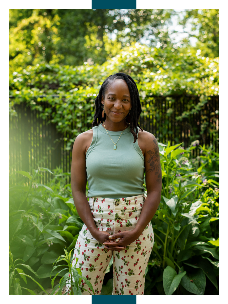 Patty Lacrete clasps her hands and smiles for the camera in a lush, leafy garden