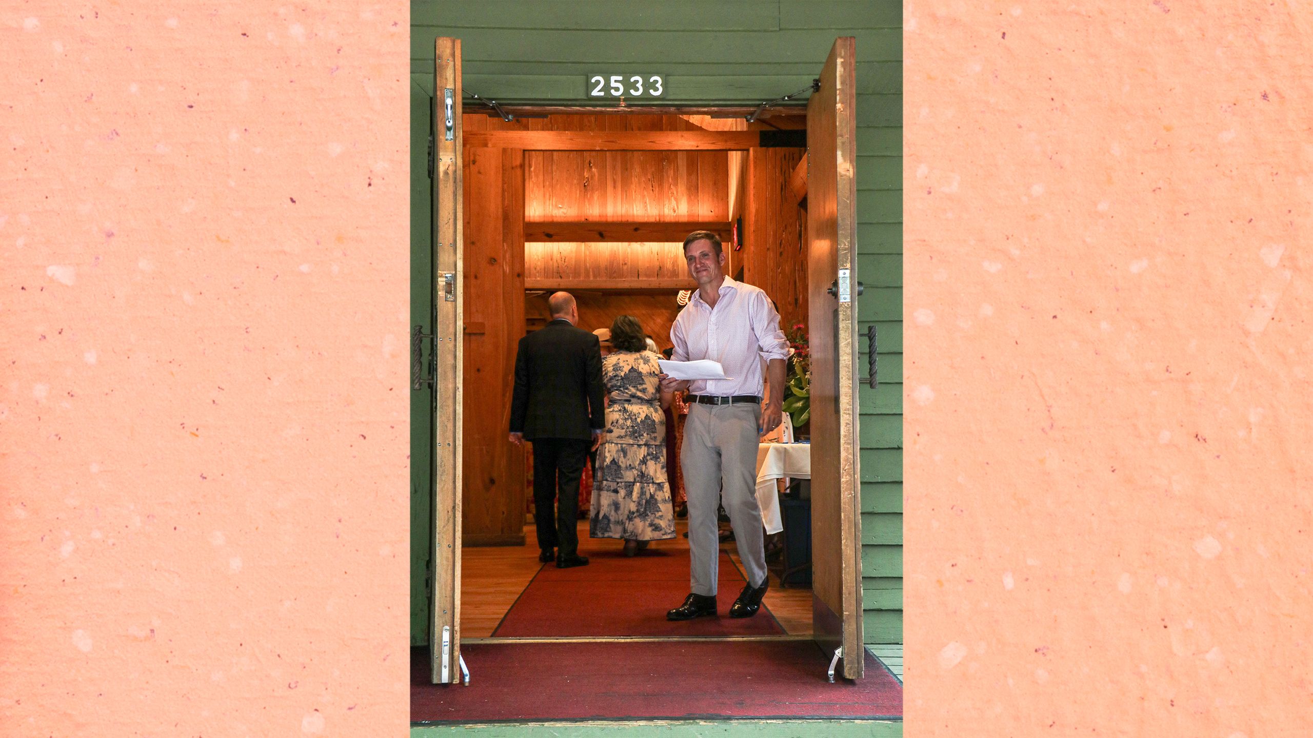 Ty Brooks wears a white shirt and khaki pants and holds a clipboard as guests enter the banquet hall.